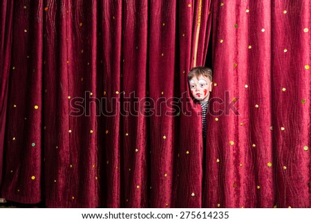Fun little boy in makeup waiting for his acting cue poking his head out between the curtains as he waits to make his entrance on stage during the performance