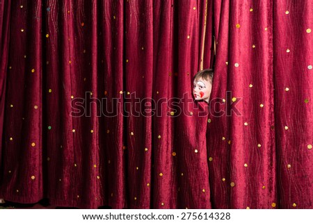 Impatient little boy on stage poking his head out from between the closed curtains as he looks to see what the delay is for the start of the play or pantomime
