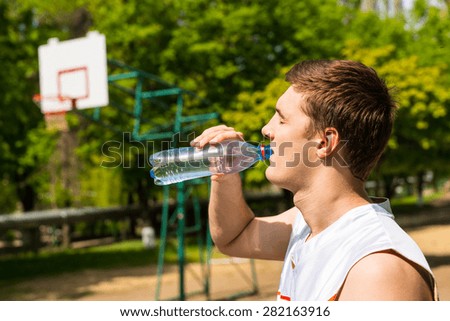 Head and Shoulders View of Young Man Drinking Water from Bottle, Taking a Break for Refreshment and Hydration on Basketball Court
