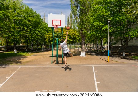 Young Athletic Man Taking Lay Up Shot on Basket on Basketball Court in Lush Green Park
