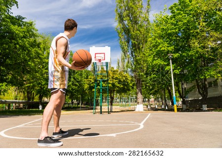 Rear View of Athletic Young Man Free Throwing Basketball from Top of Key on Outdoor Court in Lush Green Court