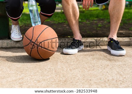 Low Angle Close Up View of Basketball on Ground at Feet of Young Athletic Couple Sitting on Park Bench After the Game