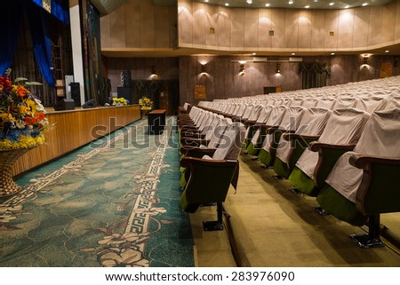 Side View of Rows of Empty Seats with Seat Covers in Well Lit Empty Theater with View of Front Row and Stage