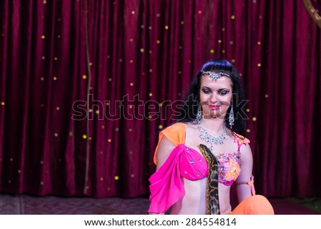 Portrait of Exotic Dark Haired Belly Dancer with Large Snake on Stage with Red Curtain in Background