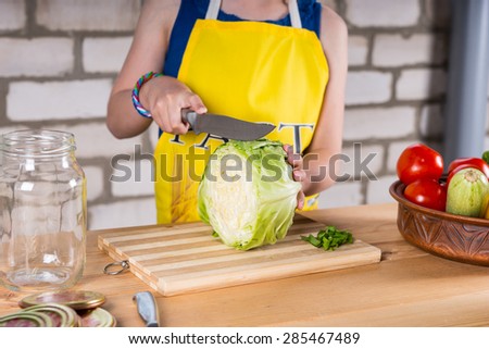 Young girl slicing fresh cabbage with a large kitchen knife on a wooden chopping board, close up of her hands