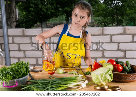 Young girl bottling colorful bell peppers placing the red and orange slices in a glass jar while working at an outdoor table