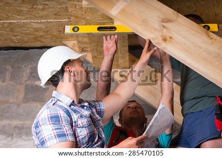 Team of Construction Workers Building Wooden Staircase, Checking Levels for Accuracy and Quality Control in Unfinished Basement of New Home