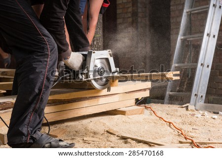 Close Up of Two Men Using Hand Held Power Saw to Cut Planks of Wood for Home Construction Leaving Piles of Saw Dust on Floor