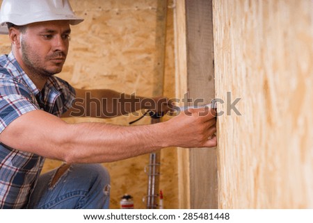 Construction Worker Builder Wearing White Hard Hat Measuring Width of Door Frame with Measuring Tape in Unfinished Home