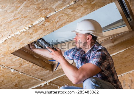 Male Construction Worker Builder Applying Fresh Caulking to Sky Light in Ceiling of Unfinished Home