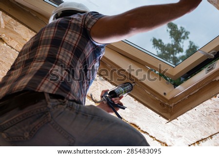 Low Angle View of Male Construction Worker Builder Applying Fresh Caulking to Sky Light in Ceiling of Unfinished Home