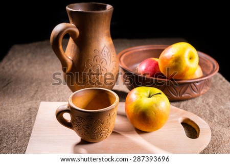 Single Apple Taken from Carved Wooden Bowl Resting on Cutting Board with Mug on Table with Pitcher in Background