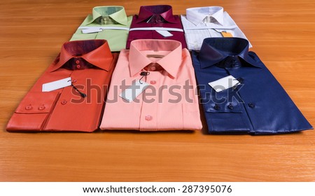 Fashion Concept Image of Collection of Six New Stylish Mens Dress Shirts Folded with Tags Attached on Wooden Surface