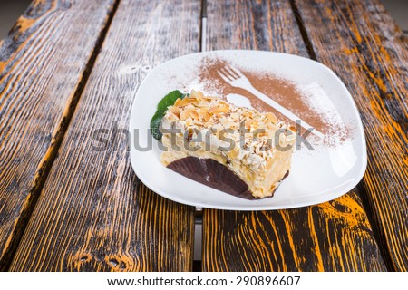Piece of Decadent Cream Cake Topped with Nuts Served on White Platter and Garnished with Mint Leaves and Cocoa Dusting on Wooden Table Surface
