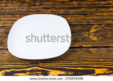 High angle view of an empty plain white ceramic plate on a textured wood background with copyspace for placement of your food or product