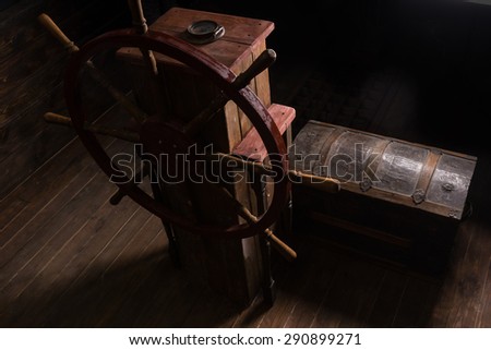 High Angle Chiarascuro of Antique Steering Helm with Wheel and Compass on Deck of Sailing Ship with Old Wooden Chest