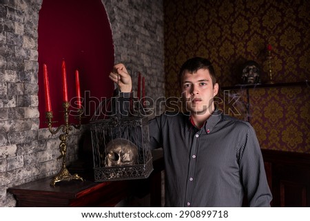 Portrait of Young Business Man Wearing Pin Striped Dress Shirt and Holding Ornate Metal Cage with Shiny Skull Inside Eerie Room of Stone Castle