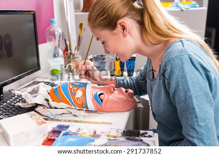 Close Up of Young Artistic Woman Carefully Painting Colorful Details onto Clay Mask at Computer Desk
