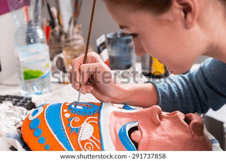 Close Up of Young Artistic Woman Carefully Painting Colorful Details onto Clay Mask in Art Class