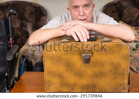 Senior Tailor Guy with Special Needs, Leaning on his Vintage Sewing Machine Case and Looking at the Camera.