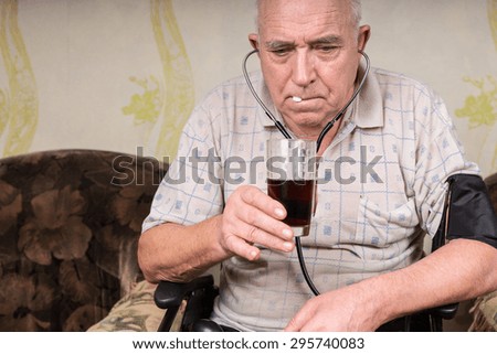 Close up Senior Bald Man with BP Apparatus Attached on his Body, Taking his Medicine with a Glass of Juice at the Living Room..