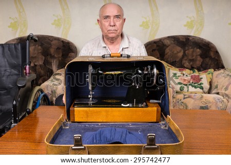 Serious Old Bald Tailor Man Sitting Behind an Open Sewing Machine Carrying Case In the Living Room.