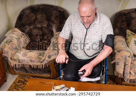 High Angle View of an Elderly Man with Special Needs Sitting on his Wheelchair, Checking his Blood Pressure Using a Manual BP Apparatus inside his House.