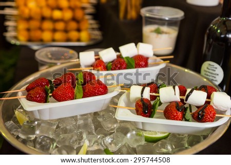 Individual Dessert Kebabs of Strawberries and Marshmallows Drizzled with Chocolate Sauce Served in Take Out Trays and Keeping Cool in Bowl of Ice on Buffet Table
