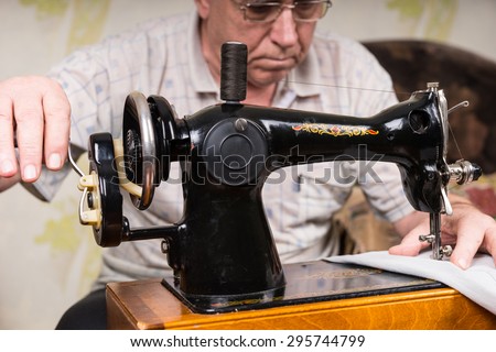 Close Up of Senior Man Using Manual Old Fashioned Sewing Machine to Mend Pants at Home