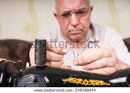 Close Up of Senior Man in Deep Concentration Threading Needle of Old Fashioned Manual Sewing Machine