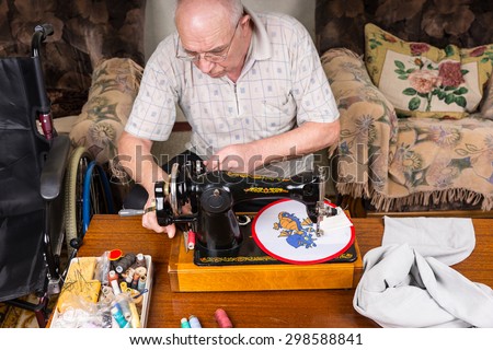 High Angle View of Senior Man Working on Needle Point Wall Hanging Using Old Fashioned Manual Sewing Machine at Home in Living Room