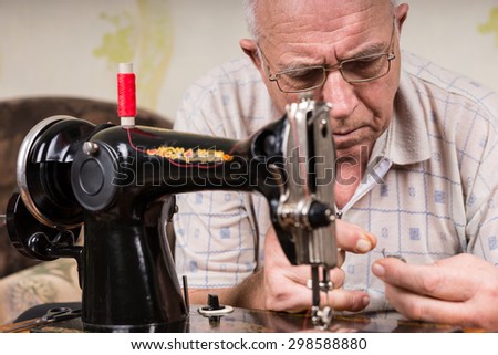 Close Up of Senior Man Threading Old Fashioned Manual Sewing Machine with Red Thread