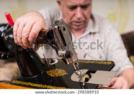 Close Up of Senior Man Inspecting Bottom of Old Fashioned Sewing Machine in Living Room at Home