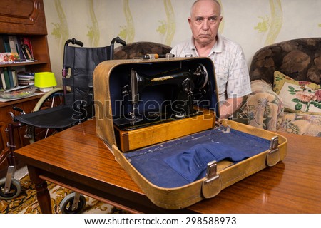 Serious Senior Tailor Man Showing his Manual Sewing Machine Inside a Carrying Case on Top of the Table in the Living Room.