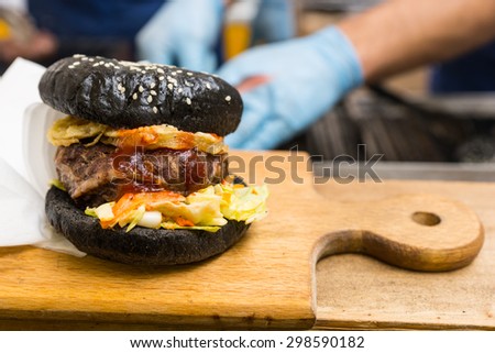 Close Up of Gourmet Burger Served on Wooden Cutting Board with Copy Space and People in Background