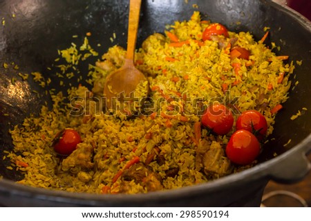 Close Up of Aromatic Yellow Rice Dish Made with Fresh Tomatoes and Vegetables Cooking in Large Pot with Wooden Spoon