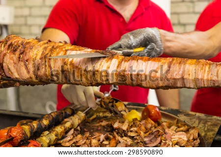 Two chefs carving a spit roast over a barbecue fire using a sharp kitchen knife to slice of thin slices for a buffet or takeaway menu