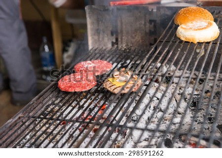 Close Up of Burger Patties Cooking on Hot Charcoal Barbecue Grill with Bun Toasting on Top Rack