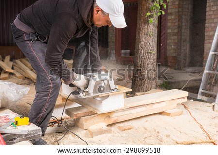 Man Using Hand Held Power Saw to Cut Planks of Wood for Home Construction Leaving Piles of Saw Dust on Floor