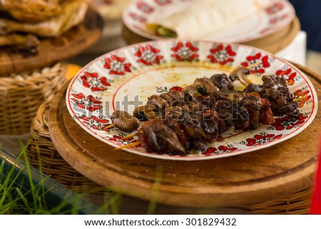 Close Up of Two Left Over Grilled Kebab Skewers on Floral Print Plate on Table Amongst Other Dishes
