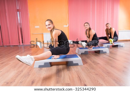 Full Length Side Profile View of Small Group of Three Smiling Young Women Balancing on Hands with Raised Legs on Step Platforms in Aerobic Class in Dance Studio with Hardwood Floor