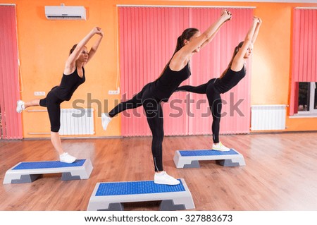 Three Fit Girls Doing Balance Exercise with One Leg on Top of Aerobic Step Platforms Inside the Gym.