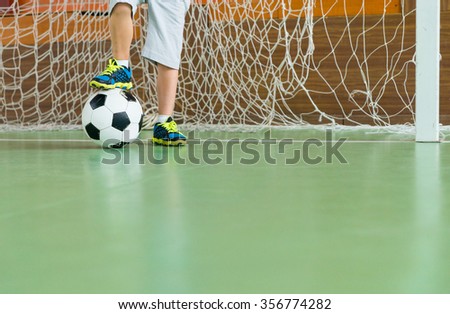 Young goalkeeper on an indoor court standing with one foot resting on the soccer ball, low angle view of his legs with copy space