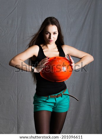 beautiful girl black t-shirt and Turquoise shorts on gray background with orange worker helmet in hands