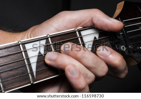 Close up shot of a man with his fingers on the frets of a guitar