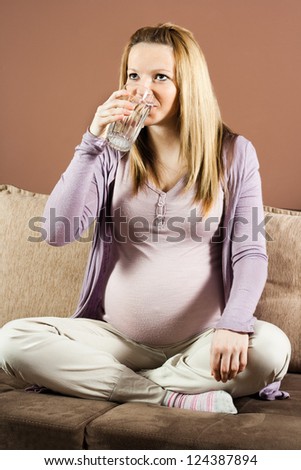 Pregnant woman sitting on the sofa and drinking water,Healthy refreshment