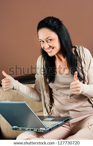Young woman sitting on the sofa with her laptop and holding thumbs up,Young woman using laptop