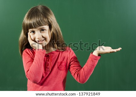 Cute little girl holding or showing your product in front of blackboard,Little girl holding your product