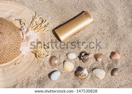 Photo of suntan lotion bottle with straw hat, shells and rocks in the sand