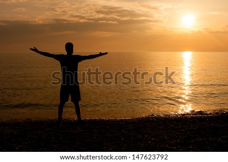Man with his arms outstretched at the beach looking at sunset